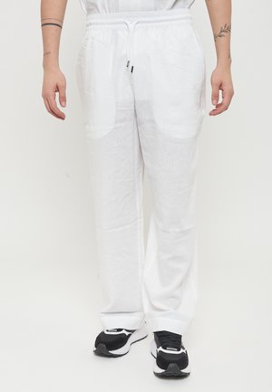 Pantaloni di lino bianchi con vestibilità rilassata, dotati di una vita elasticizzata con coulisse e tasche laterali. Indossati con sneakers in bianco e nero.