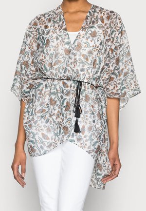 Top estilo kimono floral con mangas anchas, cinturón negro con borlas, usado sobre pantalones blancos y una camiseta interior blanca.