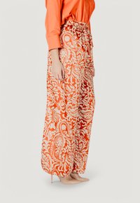 Oranje broeken met paisleypatroon en wijde pijpen, voorzien van een elastische tailleband, gecombineerd met nude hakken. Soepele stof met een vloeiende textuur.