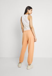 Lichte oranje joggers met elastische boorden, gecombineerd met een witte tanktop. De outfit heeft een relaxte pasvorm en een zachte textuur.