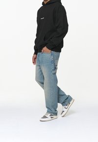 Svart hoodies med framficka, ljusblå baggy jeans med sidofickor, och vita sneakers med grå detaljer.