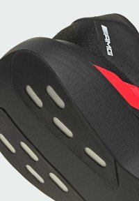 Black and red sneaker with a textured upper, rubber sole, and unique accent patterns. Features a smooth heel and visible tread sections.
