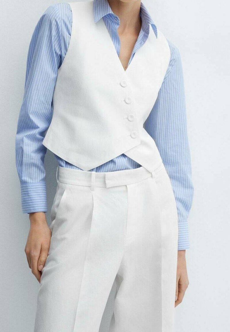 Gilet bianco su misura con chiusura a bottoni, indossato sopra una camicia a righe azzurre chiare, abbinato a pantaloni bianchi con pieghe nette.