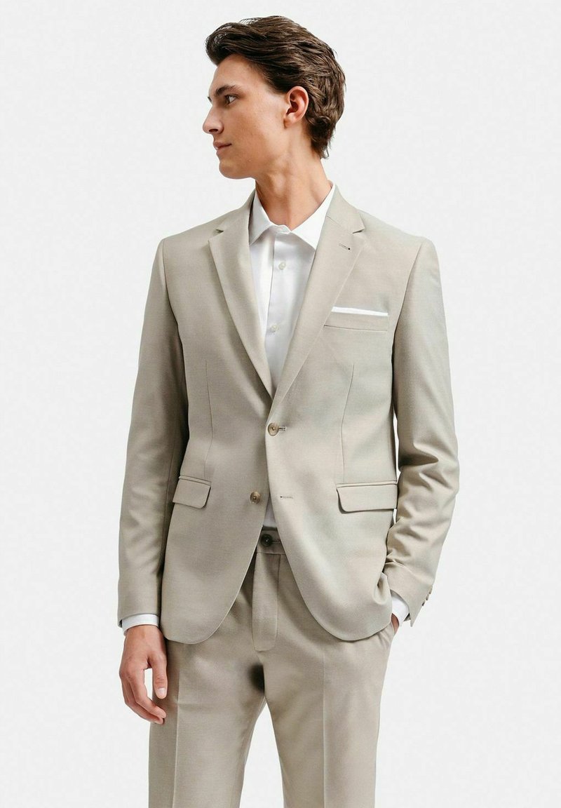 Ljusbeige kostym med skräddarsydd passform, som har en ensidig kavaj, med snedskurna slag och en vit skjorta under.