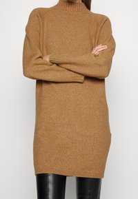 Pletený rolák v teplé béžové, s volnějším střihem, s žebrovanými manžetami a lemem, vyrobený z měkké tkaniny s jemnou strukturou.