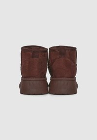 Bottines en suède marron avec une finition texturée, bout rond et semelles en caoutchouc. Elles disposent de poignées pour un enfilage facile.