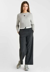 Pull en maille côtelée gris clair avec un petit logo noir, associé à un pantalon noir à rayures fines doté d'une taille élastique et de poches. Baskets argentées.