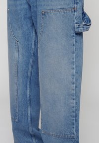 Pantalones cargo de denim azul con dos bolsillos de parche, un corte relajado, costuras visibles y un lazo para llevar accesorios.