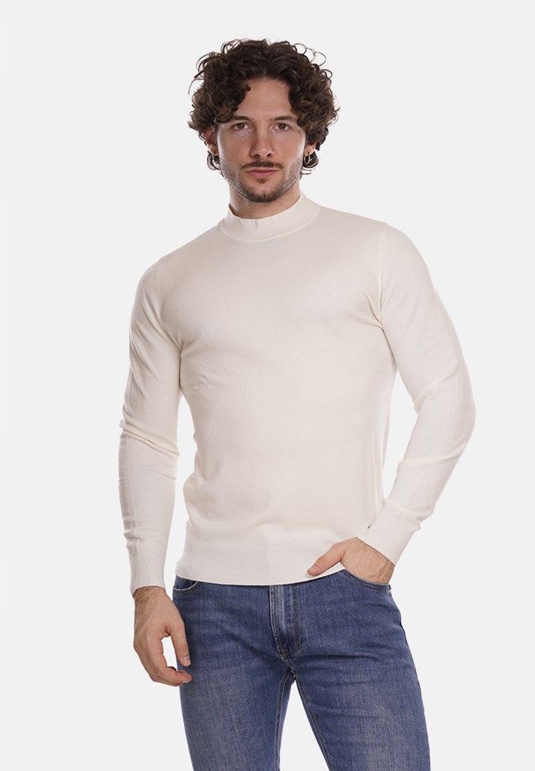 Maglione a collo alto crema con maniche lunghe. Tessuto a maglia liscio, design aderente, polsini e orlo a costine, abbinato a jeans blu.