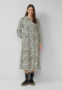Abito a maniche lunghe, con colletto, di colore crema con macchie leopardate nere. Presenta un design a strati e una vita elasticizzata. Abbinato a stivali neri chunky.