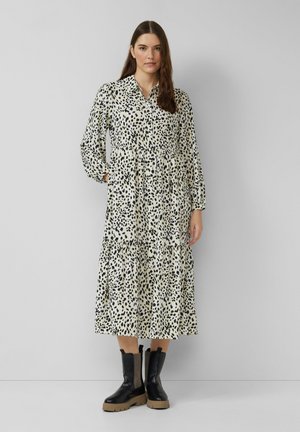 Korte mouw, geklede jurk in crème met zwarte luipaardvlekken. Kenmerken zijn het gelaagde ontwerp en de elastische taille. Gekomplementeerd met dikke zwarte laarzen.
