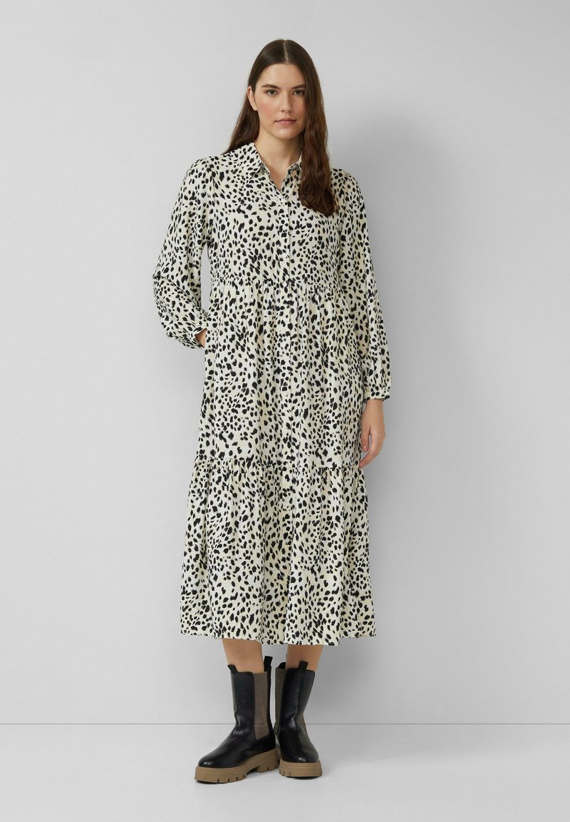 Langärmliges, kragenloses Kleid in Creme mit schwarzen Leopardenflecken. Verfügt über ein gestuftes Design und einen elastischen Bund. Kombiniert mit schwarzen, klobigen Stiefeln.