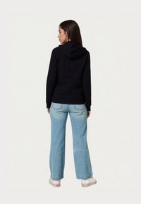 Fekete kapucnis felső kenguru zsebből, bordázott mandzsettákkal és aljjal; világoskék bőszárú farmerral és fehér platform sportcipővel párosítva.