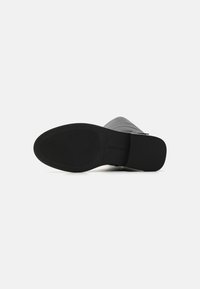 Semelle noire d'une botte en cuir avec talon carré, vue par le dessous sur un fond blanc uni.
