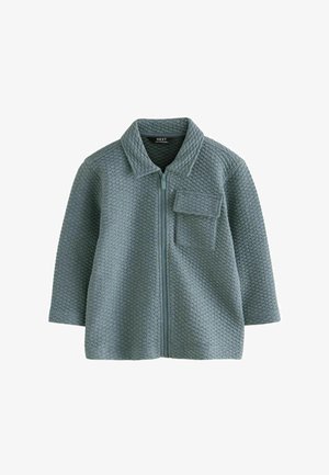 Lyseblå zip-up jakke lavet af tekstureret stof med et honningkombinationsmønster, der har en krave og en frontlomme.