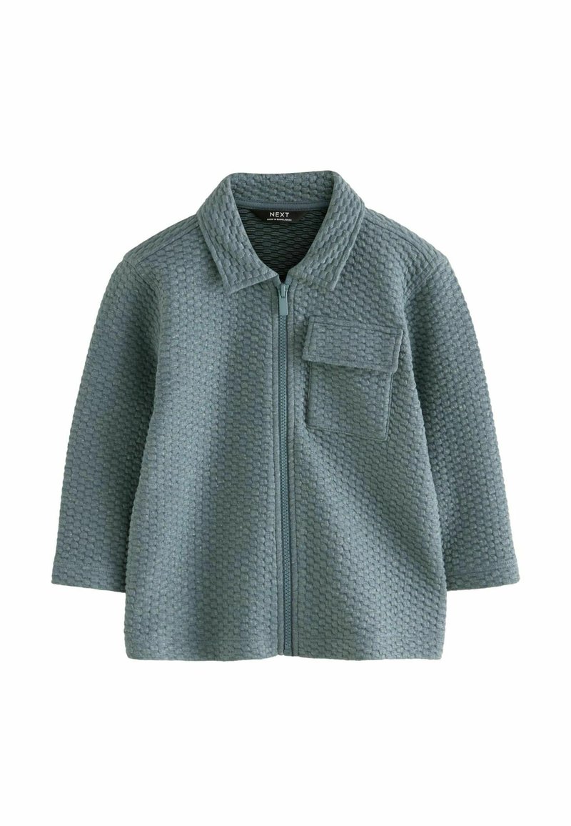 Ljusblå zip-up jacka gjord av texturerat tyg med ett bikake-mönster, utrustad med krage och en framficka.