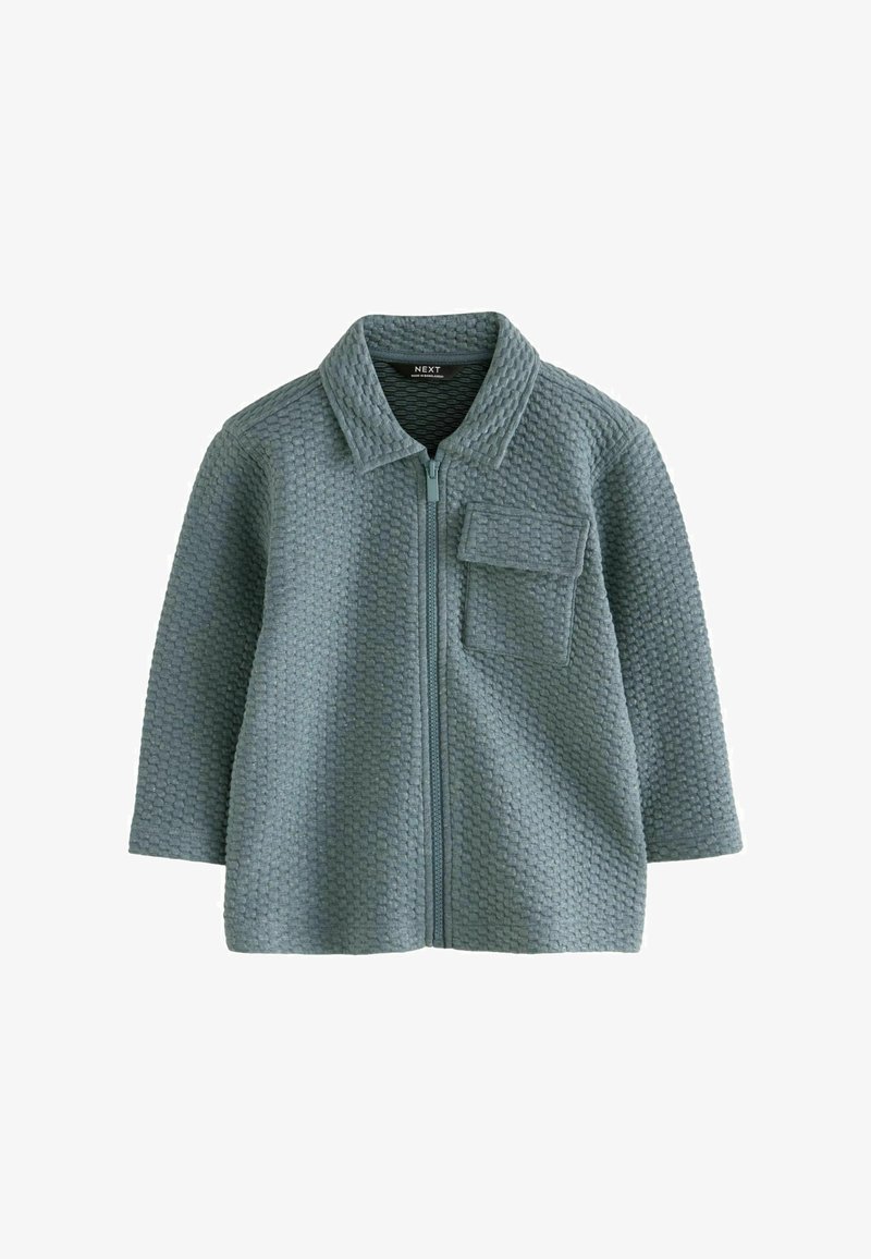 Svetlo modrá zipsová bunda vyrobená z tkaniny s textúrou v tvare medovej plástve, s golierom a prednou vreckom.