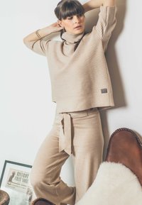 Beige gestrickter Pullover mit gerippter Textur und kurzen Ärmeln, kombiniert mit passenden hochgeschnittenen Hosen mit einem Bindegürtel.