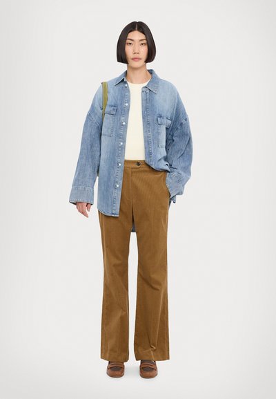 Denim särgid nupudega ees ja kahte rinna taskut, koos pruunide korduroo pükstega. Mudel kannab valget sviitr ja pruune kingi.