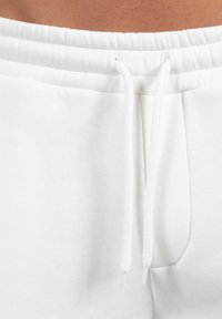 Weiße Trainingshosen verfügen über einen elastischen Bund mit Kordelzug und eine Seitentasche, gefertigt aus weichem, strukturiertem Baumwollmaterial.