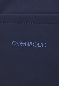 Mörkblått tyg med prydlig sömnad ovanför ljusblå text som lyder "even&odd" centrerad på materialet.