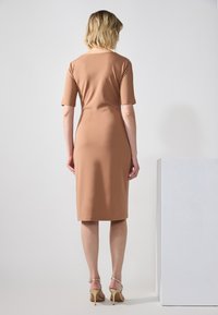 Tettende, knelengde kjole i myk beige stoff, med korte ermer og scoop rygg. Kombinert med gull ankelsko.