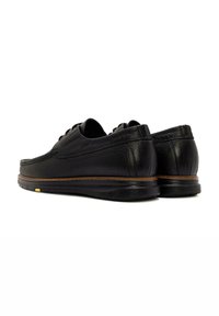 Chaussures en cuir noir avec une finition texturée, bout rond, à laçage, et un accent de semelle marron contrastant. Apparence lisse et élégante.