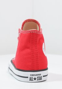 Rote Leinensneaker im High-Top-Stil mit weißen Nähten, schwarzer Gummisohle und einem runden Logopatch an der Außenseite.