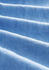 Jasnoniebieska tkanina o miękkiej teksturze, z gładkimi, równymi fałdami i lekko lśniącą powierzchnią. Brak widocznych wzorów lub akcentów.