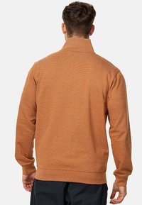 Pull à motif orange, featuring un col haut, des manches longues, des poignets et un ourlet côtelés. Fabriqué en tissu tricoté texturé.