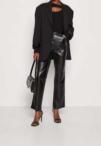 Blazer oversize nero su una canotta nera a costine, abbinato a pantaloni in pelle nera con vita alta e sandali con tacco neri e cinturini.