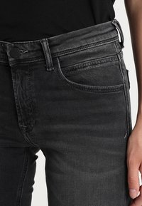 Jeans negros de mezclilla, con un corte ajustado, diseño clásico de cinco bolsillos y detalles desgastados alrededor de la cintura y los bordes de los bolsillos.