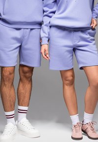 Světle fialové trička ze směsi bavlny a šortky, s uvolněným střihem, žebrovanými manžetami a viditelnými švy. Bílé a růžové tenisky.