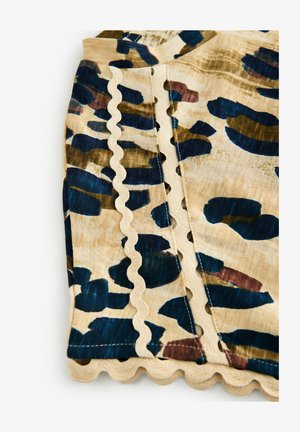 Tan stof med blå, grønne og bordeaux abstrakte mønstre, med en bølget kant og kontrastsygning langs sømmene.