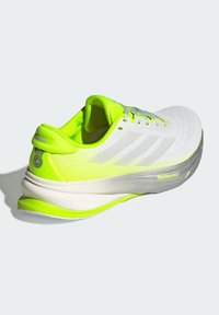 Weiße Laufschuhe mit neon-gelben Akzenten, Mesh-Obermaterial, strukturierten Sohlen und sichtbarem Markenlogo. Verfügt über eine gepolsterte Ferse für zusätzlichen Halt.