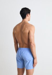 Shorts de bain bleu clair avec ceinture élastique, poche à l'arrière et texture lisse, montrés de dos sur un torse nu.