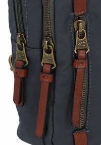 Bolso de tela en azul marino oscuro que presenta tres cremalleras de color bronce con tiradores de cuero marrón, destacado por costuras visibles y acentos texturizados.