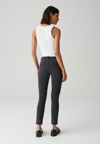 Jean en denim noir avec une coupe ajustée, poches avant et coutures visibles. Associé à un débardeur blanc. Texture lisse, longueur cheville.