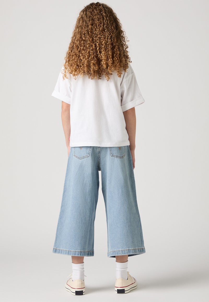 T-shirt bianco a maniche corte, culotte in denim light blue a taglio largo, lunghezza alla caviglia, con orli arrotolati, indossate con calze bianche e sneakers beige.