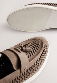 Light brown leather slip-on shoes with woven texture and tassel detail; rubber outsole with horizontal ridges; round toe design.