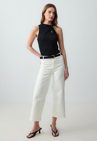 Zwart mouwloos bodysuit met een keyhole-detail, gecombineerd met witte wijde broek en zwarte hoge sandalen; gladde, aansluitende stof.