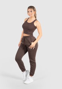 Brun ribbad crop top i kombination med matchande joggerbyxor, med elastiska manschetter och fickor. Modellen bär vita träningsskor.