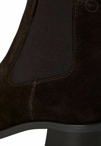 Gros plan d'une botte Chelsea en daim marron foncé avec panneau latéral élastique et semelle en caoutchouc noir.