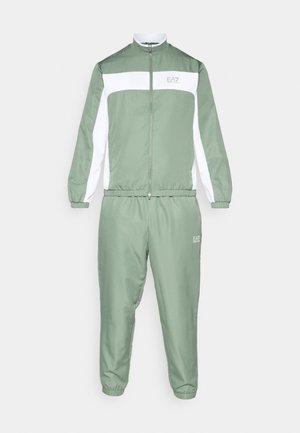 Αθλητική φόρμα σε ανοιχτό πράσινο, με μπουφάν με φερμουάρ και λευκές λεπτομέρειες, ελαστικά μανίκια, συνδυασμένη με αντίστοιχο στενό παντελόνι. Εμφανίζεται το λογότυπο "EA7".