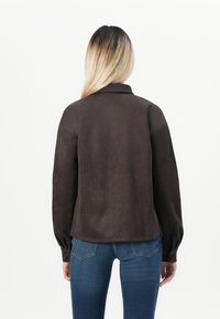 Brown suede jacket with a collar and long sleeves, featuring button accents and a tailored fit, paired with blue jeans.