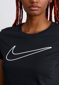 Pessoa com cabelo vermelho trançado vestindo uma t-shirt preta com um grande logotipo branco da Nike em forma de swoosh no peito.