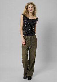 Top senza maniche nero con scollatura drappeggiata e motivo a pois argento, abbinato a pantaloni larghi verde oliva e scarpe nere.
