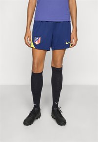 Navy atletikshorts med gule detaljer og Atletico Madrid-logo, kombinert med svarte knelange sokker og svarte fotballsko.