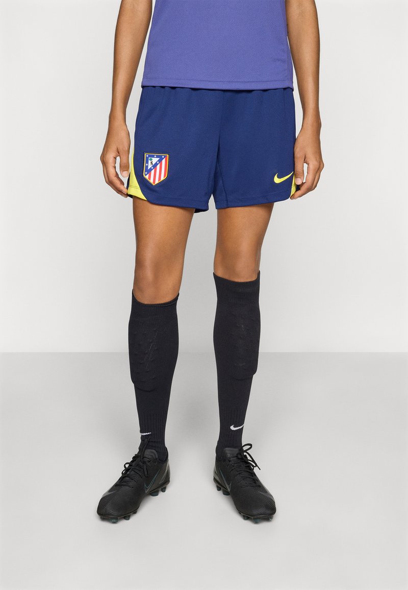 Navy atletikshorts med gule detaljer og Atletico Madrid-logo, kombinert med svarte knelange sokker og svarte fotballsko.