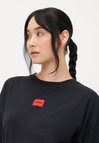 Zwart oversized t-shirt met een rode rechthoekige tag met het "HUGO"-logo. Glad katoen, ronde halslijn, ontspannen pasvorm, korte mouwen.